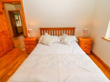 A bedroom with a wooden double bed two nightstands with lamps and a doorway at Mary Agnes Cottage in Cahirkeen near Allihies County Cork