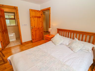 A bedroom with a wooden bed and side table with lamp near two wooden doors at Mary Agnes Cottage in Cahirkeen near Allihies County Cork