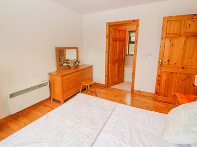 A bedroom with a wooden dresser mirror stool and an open door showing a bathroom at Mary Agnes Cottage in Cahirkeen near Allihies County Cork
