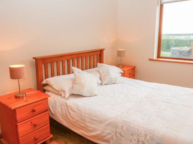 A bedroom with a wooden bed and two wooden bedside tables with lamps at Mary Agnes Cottage in Cahirkeen near Allihies County Cork