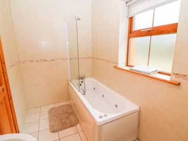 A bathroom with a bathtub a small beige rug by the tub and a window with a blind at Mary Agnes Cottage in Cahirkeen near Allihies County Cork