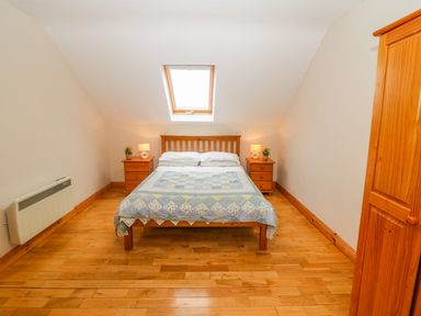 A bedroom with a wooden bed under a skylight window two bedside tables with lamps and plants and a wooden wardrobe at Mary Agnes Cottage Cahirkeen near Allihies County Cork