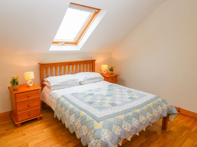 A bedroom with a wooden bed under a skylight and two wooden bedside tables with lamps and plants at Mary Agnes Cottage in Cahirkeen near Allihies County Cork