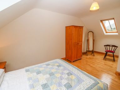 A bedroom with a bed covered in a patchwork quilt a wooden wardrobe a floor mirror a wooden chair and a skylight window at Mary Agnes Cottage in Cahirkeen near Allihies County Cork