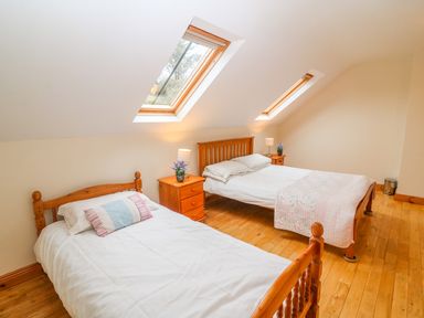 A bedroom with two wooden beds two bedside tables with lamps and plants and skylights at Mary Agnes Cottage in Cahirkeen near Allihies County Cork