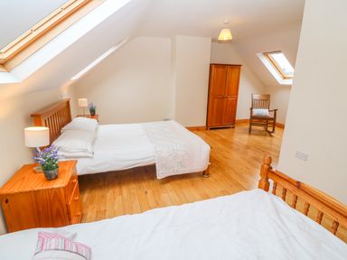 A bedroom with two beds a wooden wardrobe a rocking chair and skylight windows at Mary Agnes Cottage in Cahirkeen near Allihies County Cork