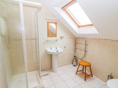 A bathroom with a shower cabin sink mirror wooden stool and a skylight window at Mary Agnes Cottage in Cahirkeen near Allihies County Cork