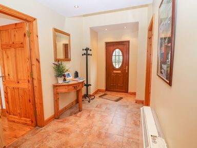 A hallway with a wooden front door a coat rack a wooden table with plants and books a mirror on the wall and a radiator at Mary Agnes Cottage in Cahirkeen near Allihies County Cork