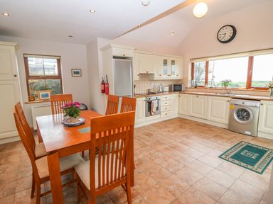 A kitchen with a wooden dining table and chairs next to cabinets appliances and a window at Mary Agnes Cottage in Cahirkeen near Allihies County Cork