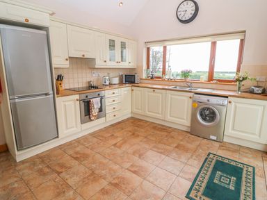 A kitchen with white cabinets a stainless steel refrigerator oven washing machine and a window over the sink at Mary Agnes Cottage in Cahirkeen near Allihies County Cork