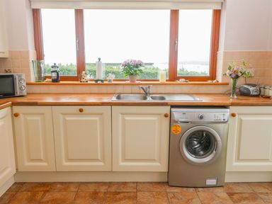 A kitchen with cream cabinets a wooden countertop a washing machine and a window with plants and decorative items at Mary Agnes Cottage in Cahirkeen near Allihies County Cork
