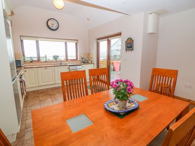 A kitchen with wooden dining table and chairs and cabinets with appliances at Mary Agnes Cottage in Cahirkeen near Allihies County Cork