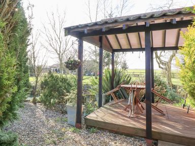 A wooden gazebo with folded chairs and table surrounded by plants and gravel at The Haybarn in Necton near Swaffham