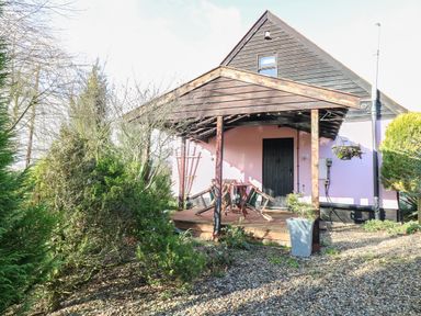 A wooden porch with a table and chairs in front of a house surrounded by trees and gravel at The Haybarn in Necton near Swaffham