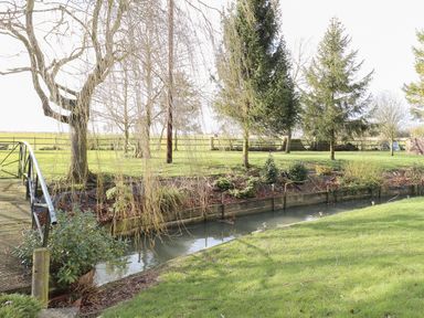 A garden with a small canal a metal bridge trees and grass at The Haybarn in Necton near Swaffham