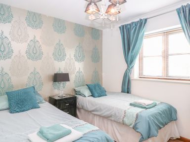 A bedroom with two single beds a nightstand with a lamp and a window with curtains at The Haybarn in Necton near Swaffham