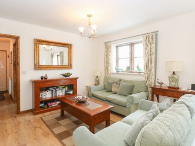 A living room with green sofas wooden coffee table bookshelves and window at The Haybarn in Necton near Swaffham