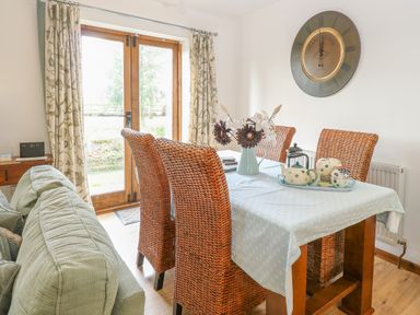 A dining area with wicker chairs a table with a blue cloth and teapot set next to a window at The Haybarn in Necton near Swaffham