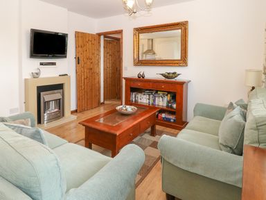 A living room with green sofas a wooden coffee table a wooden cabinet with books and board games a fireplace and a wall-mounted television at The Haybarn in Necton near Swaffham