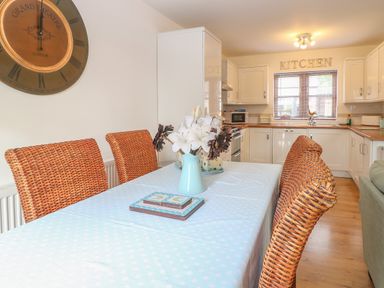 A kitchen with white cabinets a dining table with wicker chairs and a flower vase at The Haybarn in Necton near Swaffham