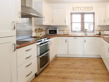 A kitchen with white cabinets wooden countertops a stainless steel oven a microwave and a window with blinds at The Haybarn in Necton near Swaffham