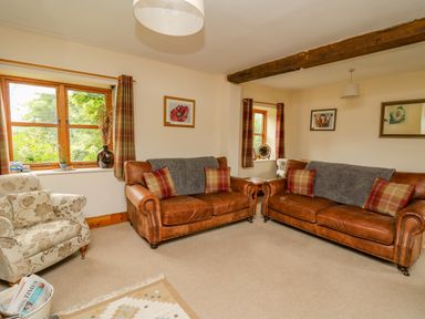 A living room with two brown leather sofas and a floral armchair at Byrdir Cottage in Rhayader