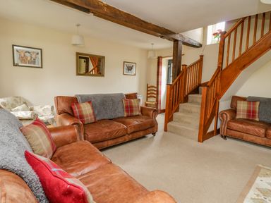 A living room with brown leather sofas and a wooden staircase at Byrdir Cottage in Rhayader