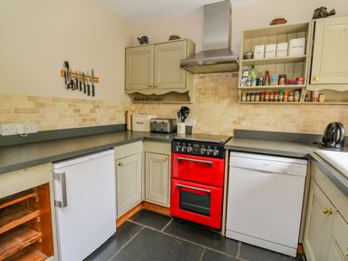 A kitchen with a red oven dishwasher refrigerator spice rack and countertop at Byrdir Cottage in Rhayader