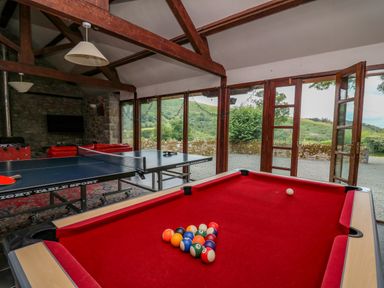 A game room with a pool table and ping pong table and large windows showing greenery outside at Byrdir Cottage in Rhayader