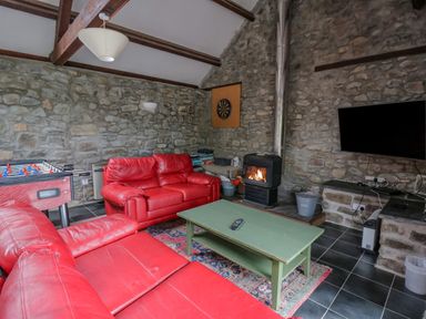 A living room with red sofas a green coffee table a foosball table and a fireplace at Byrdir Cottage in Rhayader