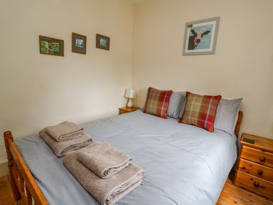 A bedroom with a double bed gray bedding red plaid pillows wooden bedside tables and folded towels at Byrdir Cottage Rhayader