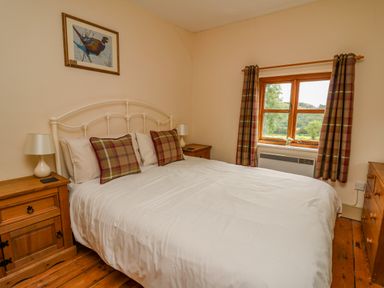 A bedroom with a white metal bed frame wooden floor bedside tables and a window with plaid curtains at Byrdir Cottage in Rhayader