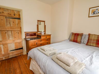 A bedroom with a bed and wooden dresser and a wooden door at Byrdir Cottage in Rhayader