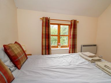 A bedroom with a bed with pillows and towels by a window with curtains at Byrdir Cottage in Rhayader