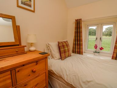 A bedroom with a single bed next to a window a dresser with a mirror and a lamp at Byrdir Cottage in Rhayader