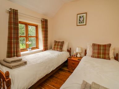 A bedroom with two single beds a window with curtains and a bedside table at Byrdir Cottage in Rhayader