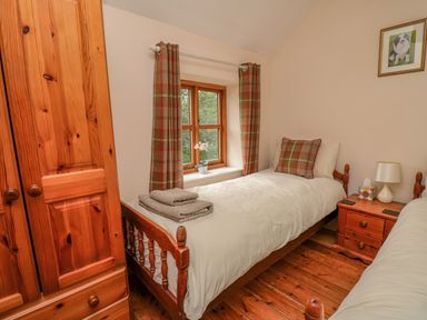 A bedroom with two single beds wooden furniture a window with curtains and a framed picture at Byrdir Cottage in Rhayader