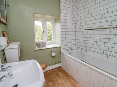 A bathroom with a bathtub, sink, toilet, window, and tiled wall at Byrdir Cottage in Rhayader