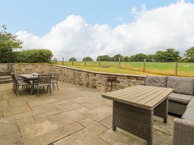 An outdoor patio with dining table and chairs and a seating area with a coffee table at Byrdir Cottage in Rhayader
