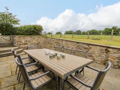 An outdoor patio with a dining table and eight chairs with cups and teapots on the table at Byrdir Cottage in Rhayader