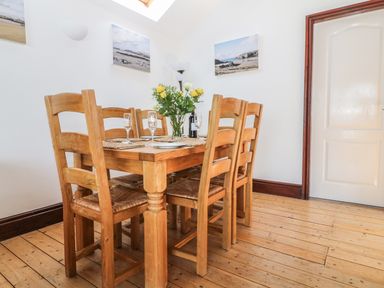 A dining area with a wooden table and six chairs a vase with flowers on the table wall art and a door at Seascape in Trearddur Bay