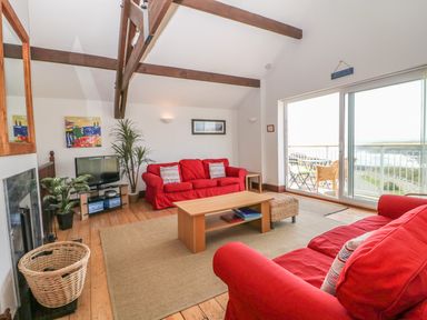 A living room with two red sofas a coffee table and sliding glass doors overlooking a balcony at Seascape in Trearddur Bay