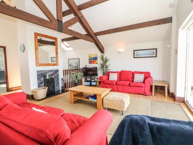 A living room with red sofas a wooden coffee table a fireplace and exposed wooden beams at Seascape in Trearddur Bay