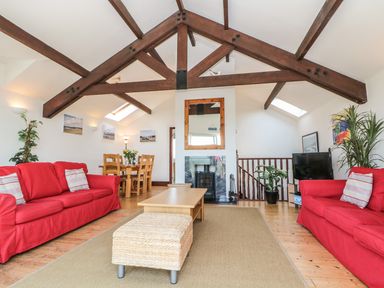 A living room with red sofas wooden beams and a dining table at Seascape in Trearddur Bay