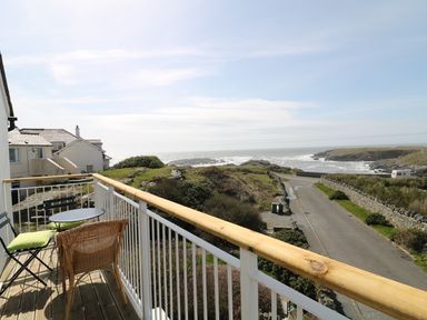 A balcony with chairs and a table overlooking a road and the coastline at Seascape in Trearddur Bay