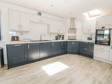 A kitchen with dark lower cabinets white upper cabinets a sink stove oven microwave and light wood flooring at Seascape in Trearddur Bay