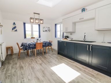 A kitchen with dining table and chairs cupboards and sink at Seascape in Trearddur Bay