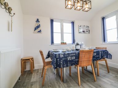 A dining area with a table covered in a blue tablecloth set with dishes and cups surrounded by four wicker chairs at Seascape in Trearddur Bay