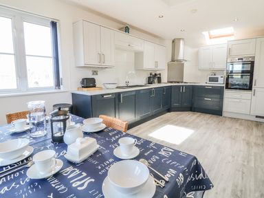 A kitchen with a dining table set with white dishes and a blue tablecloth with words at Seascape in Trearddur Bay