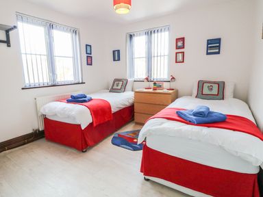 A bedroom with two single beds red bed skirts and red throws at Seascape in Trearddur Bay